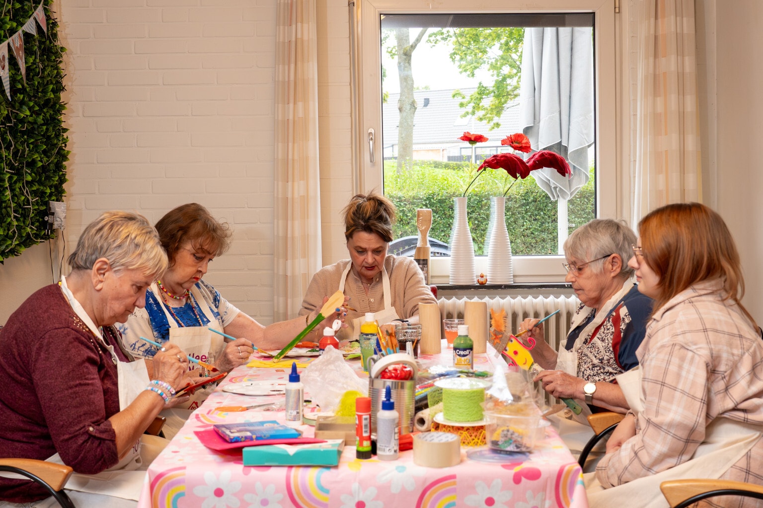 Vijf vrouwen knutselen aan een tafel waar diverse knutselspullen op staan.