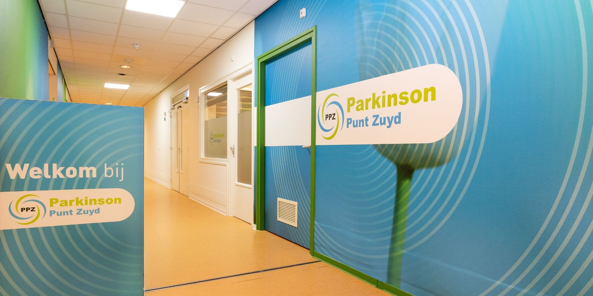 Gang in een gebouw. Op de muur staat Welkom bij Parkinson Punt Zuyd.