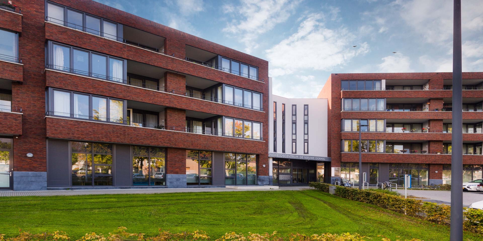 Buitenkant van een gebouw met rode bakstenen. Op de gevel staat Gezondheidscentrum De Nieuwe Dormig.