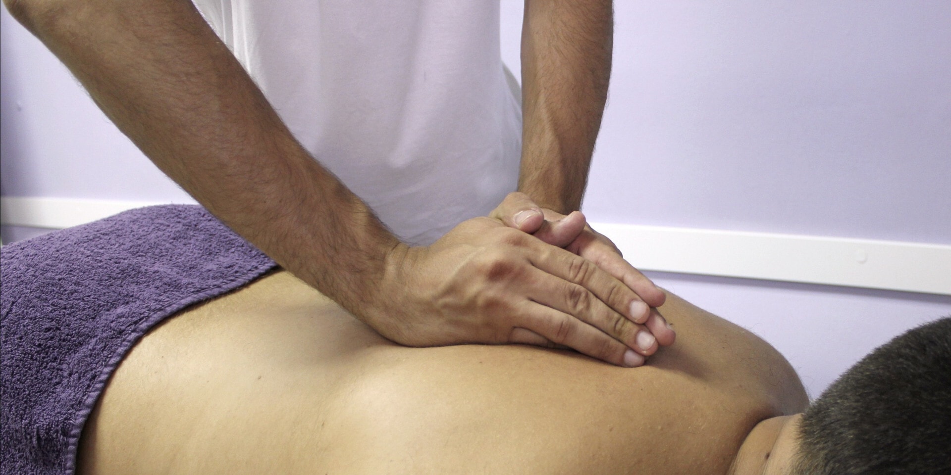 Man geeft een osteopathische behandeling aan een andere man die op zijn buik ligt.